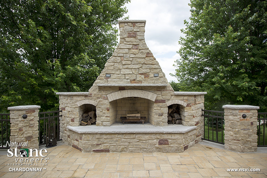 Freestanding natural stone outdoor fireplace with arched firebox and side storage niches, featuring Fond du Lac Chardonnay.