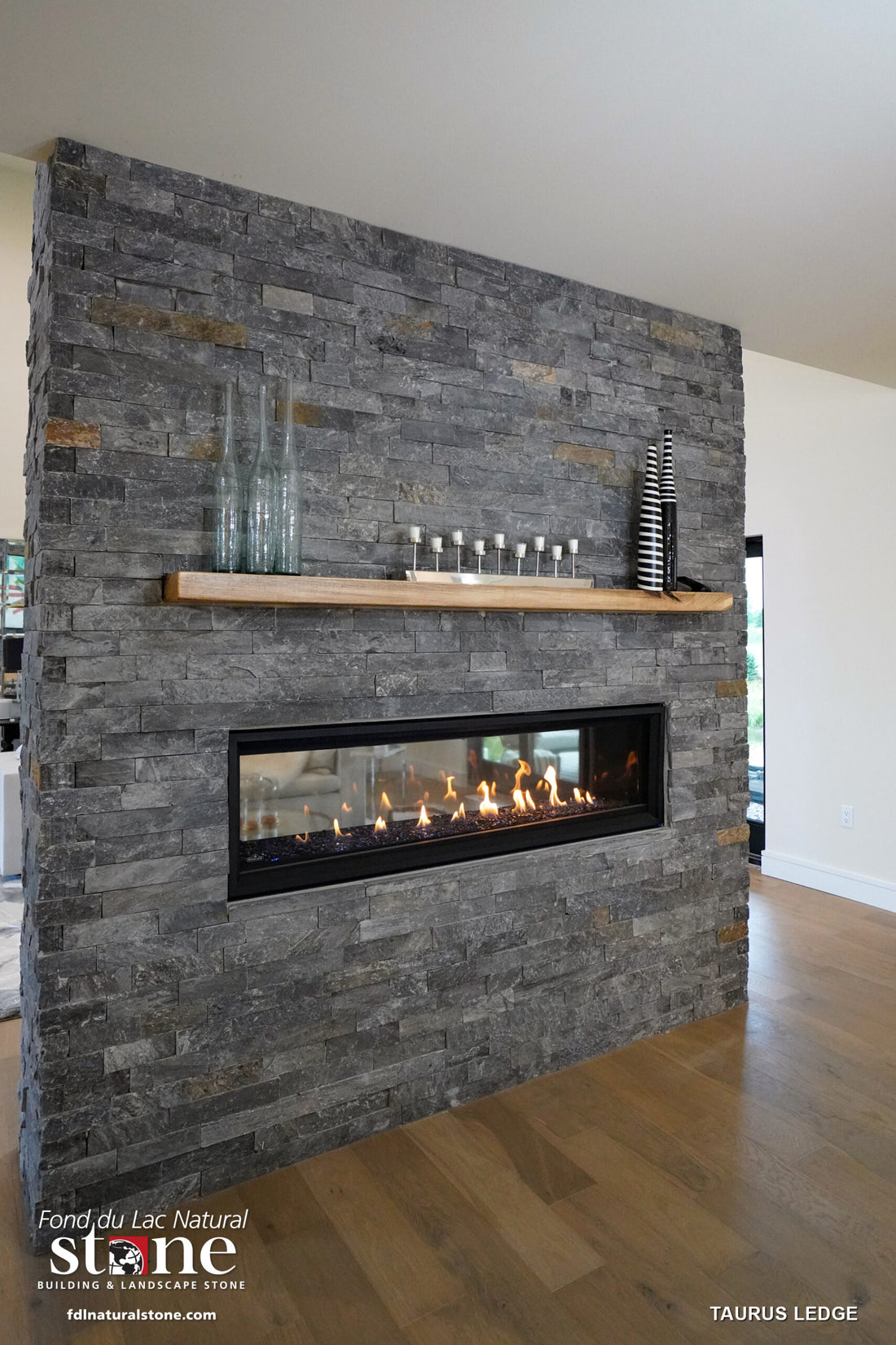 Dark natural ledgestone fireplace wall with a wood mantel and a long horizontal firebox, featuring Fond du Lac Taurus Ledge.