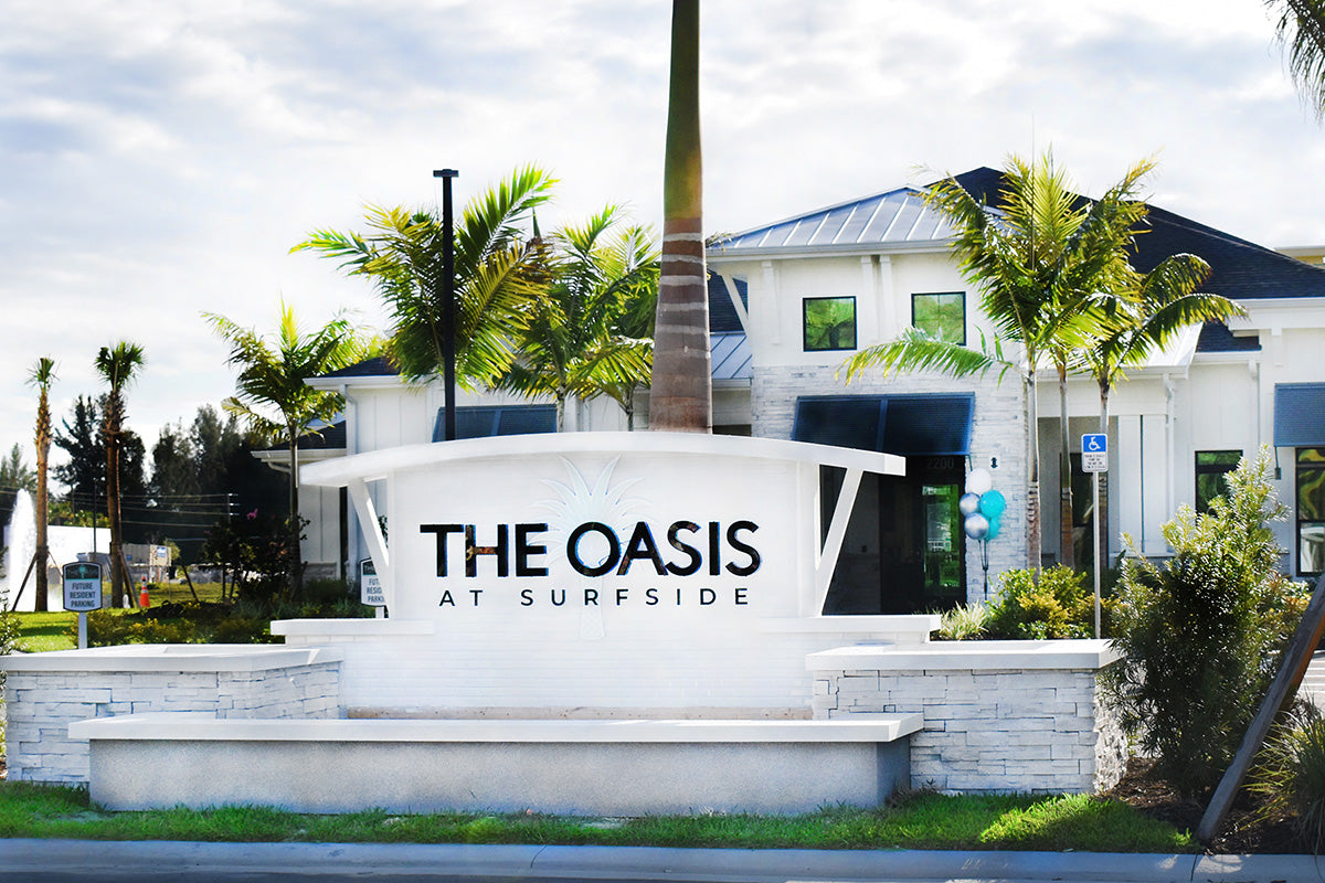 Entrance to 'The Oasis at Surfside' with palm trees and a clear sky.