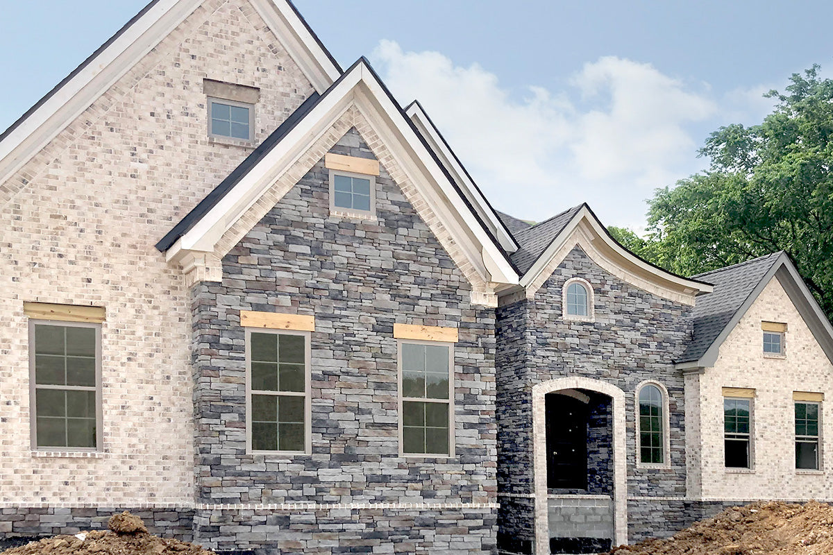 Two-story house with stone facade and white trim, surrounded by greenery.