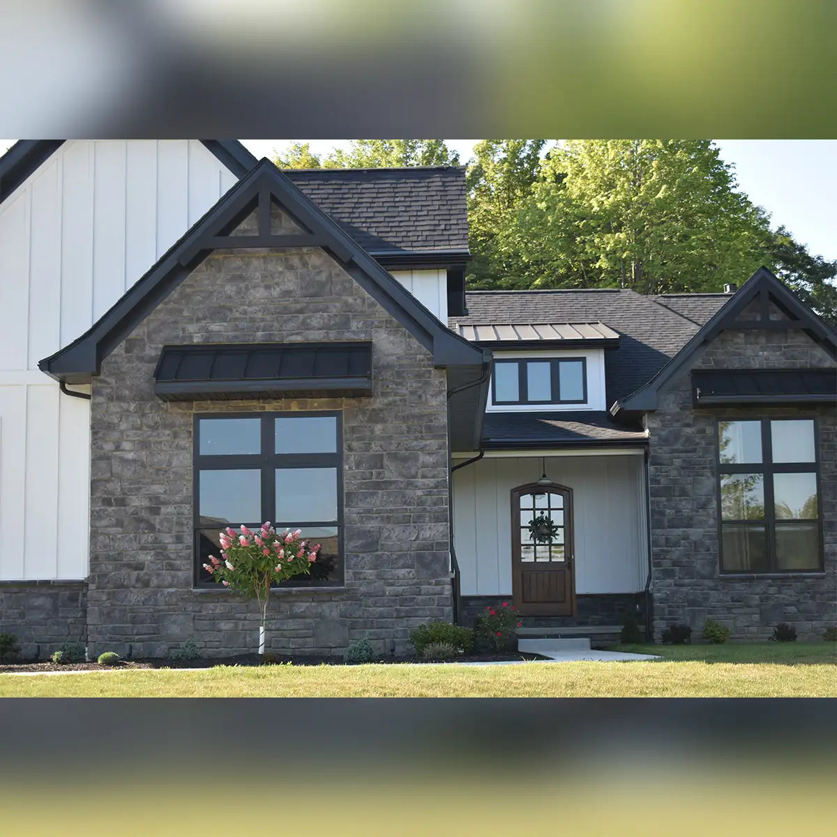 Modern stone house with black roof and white trim, featuring large windows.