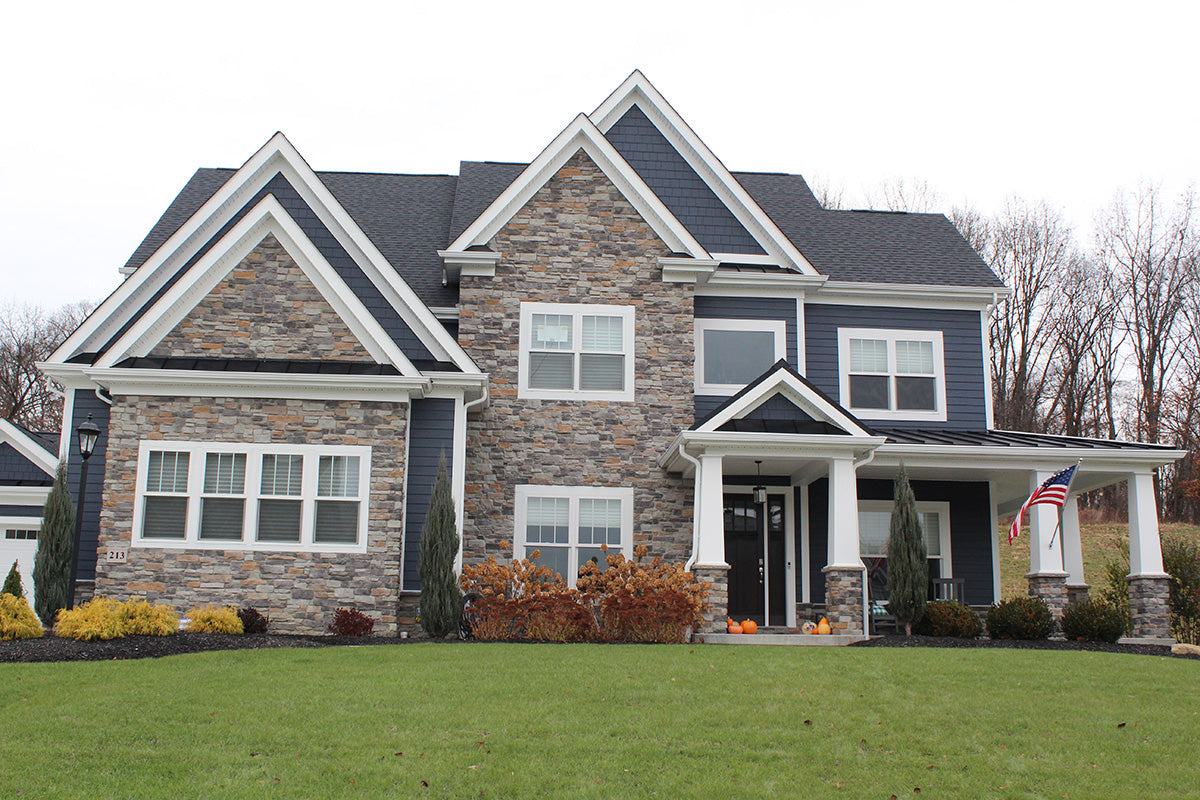 Two-story house with stone facade and blue siding on a clear day.