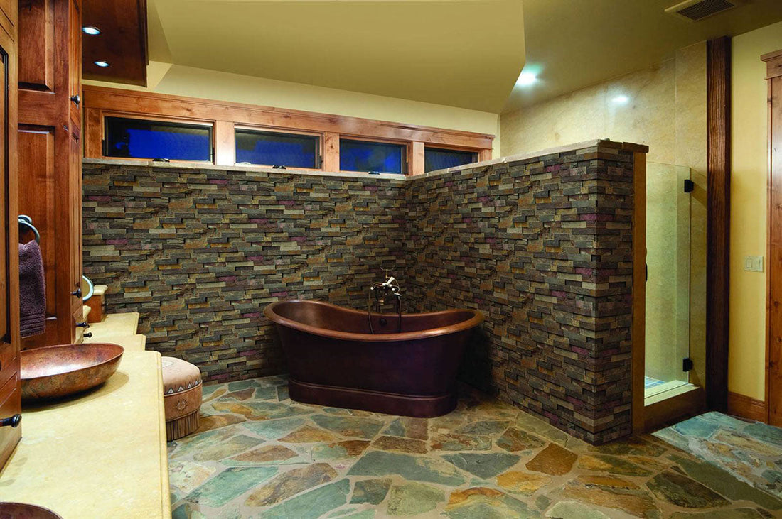 Multicolor stone panels around a dark freestanding bathtub and half-height bathroom wall, featuring MSI® Rockmount California Gold.