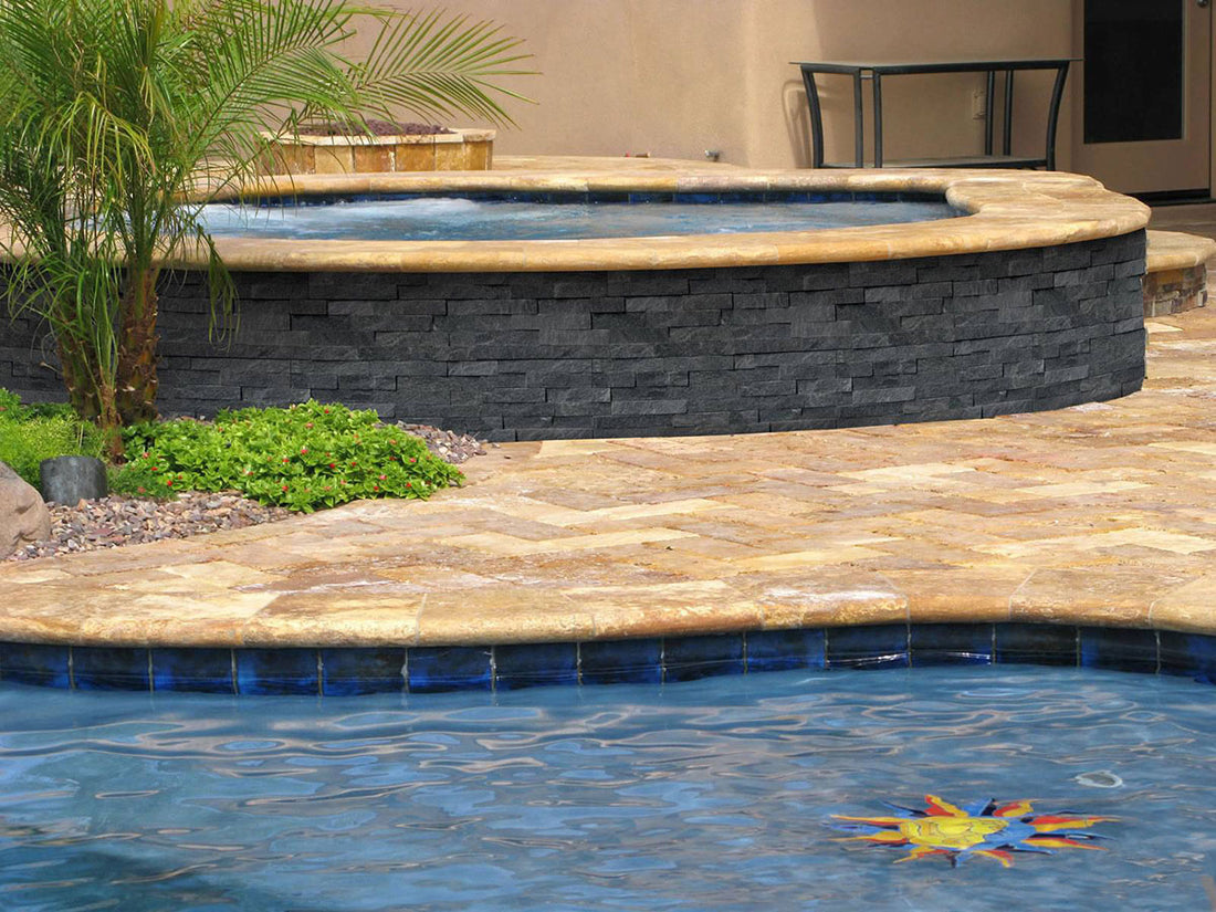 Dark natural stone panels around a raised circular spa next to a blue pool, featuring MSI® Rockmount Coal Canyon.