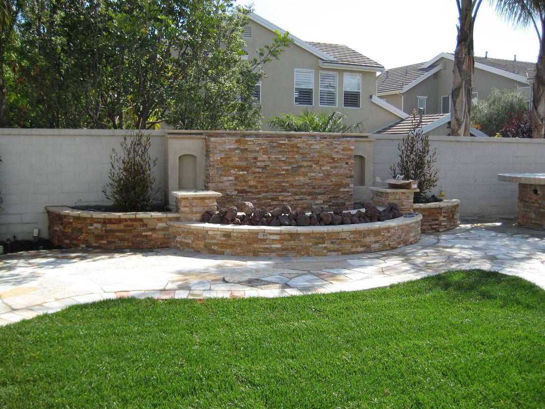 Natural stone fountain wall and curved basin beside a lawn and paved patio, featuring MSI® Rockmount Golden White.
