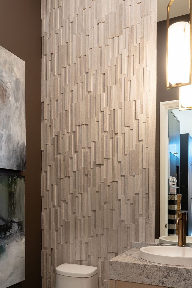 Dimensional pale natural stone panels beside a bathroom mirror, basin and wall light, featuring MSI® Rockmount White Oak 3D Honed.