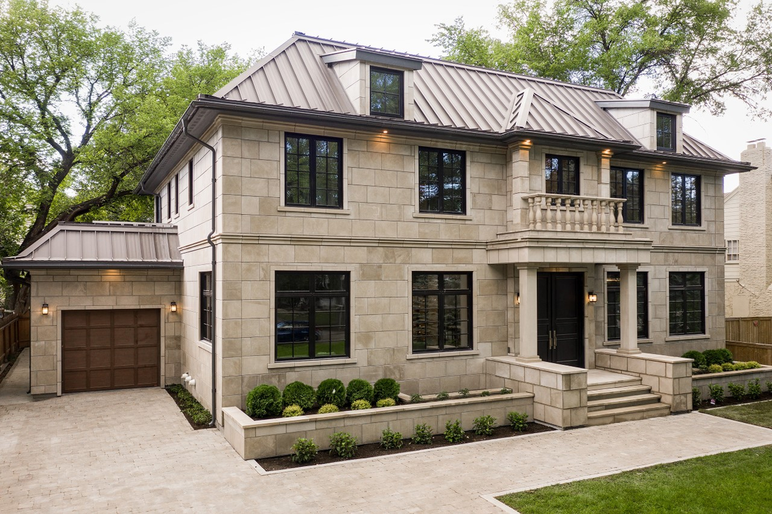 Pale limestone facade on a two-story home with dark windows and a standing-seam roof, featuring Polycor Vanderbilt Classic™ Indiana Limestone.