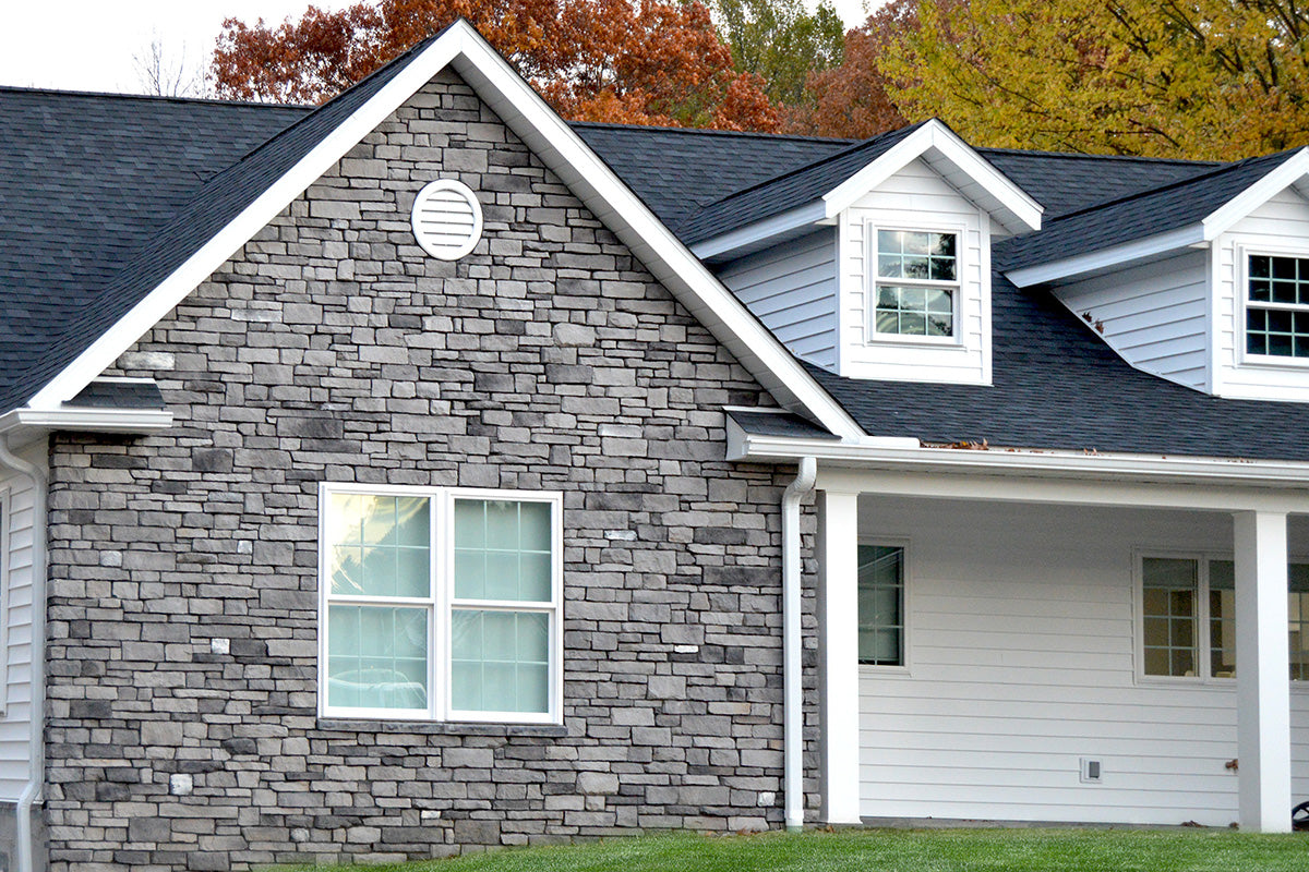 Two-story house with stone facade and white trim, surrounded by trees with autumn foliage.