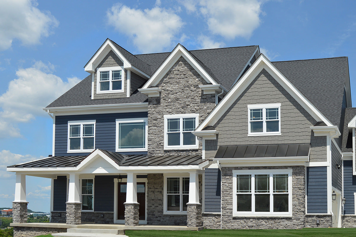 Two-story house with gray siding and white trim under a blue sky.