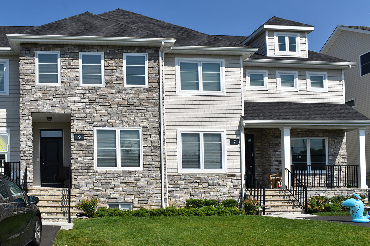 Two-story residential houses with stone and siding exteriors on a clear day.