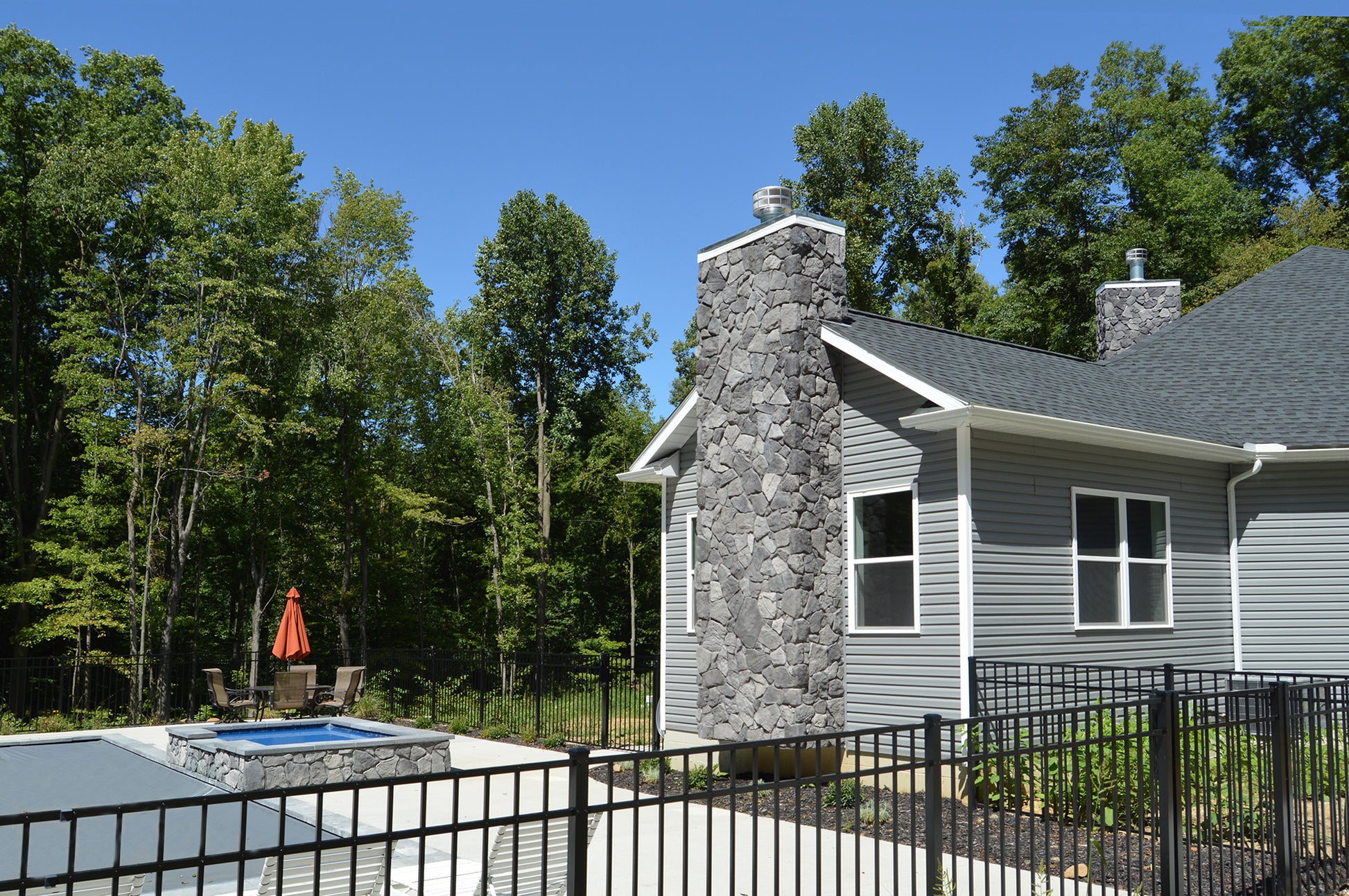 House with stone chimney and pool area surrounded by trees