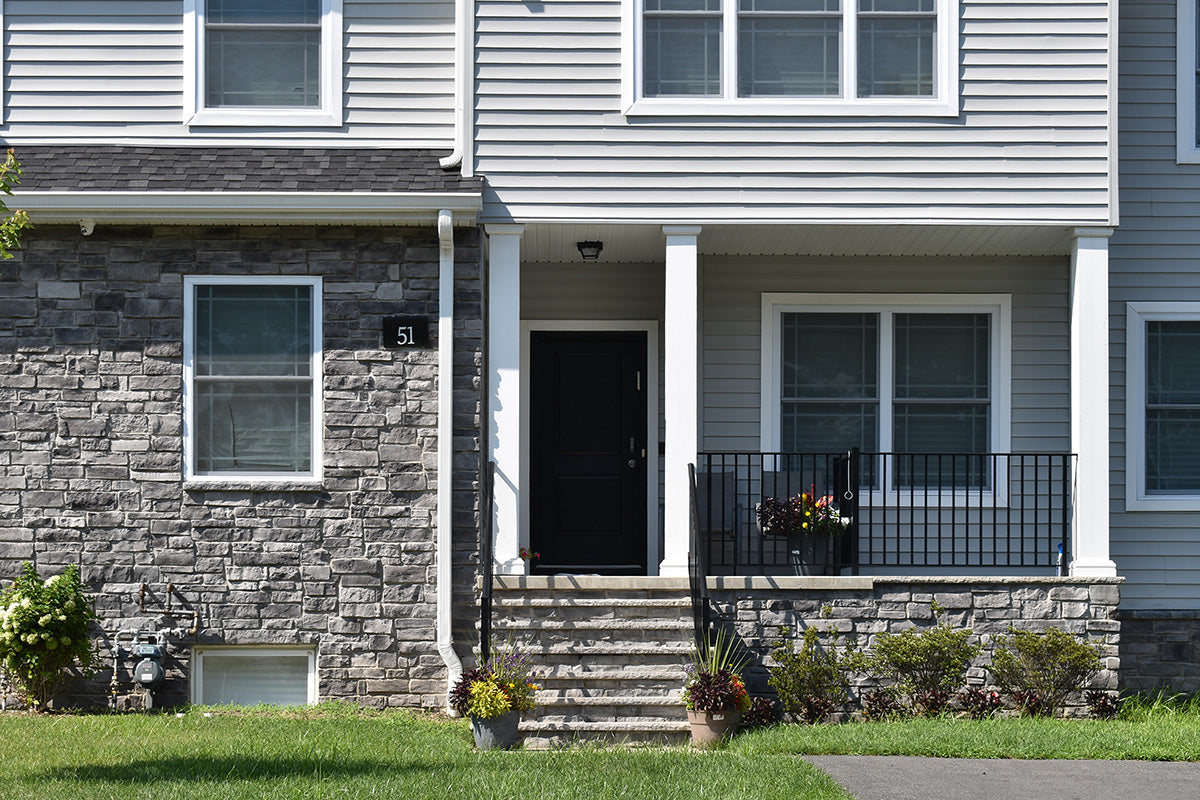 Front of a two-story house with a black door and stone porch.