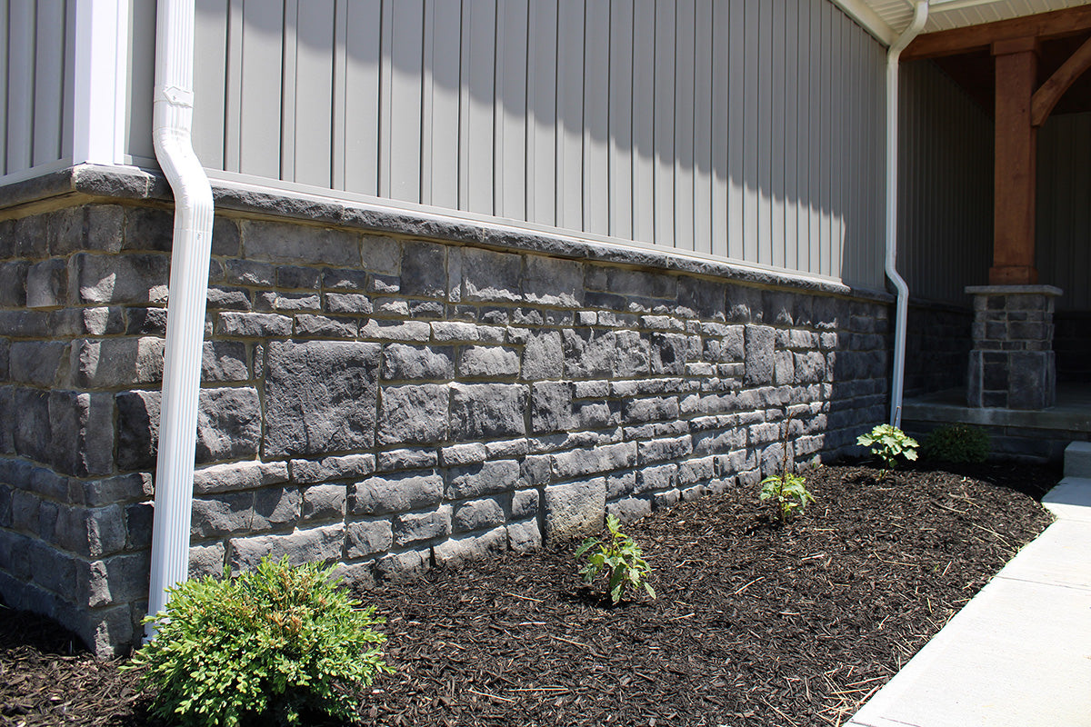 Stone wall with plants and a house in the background