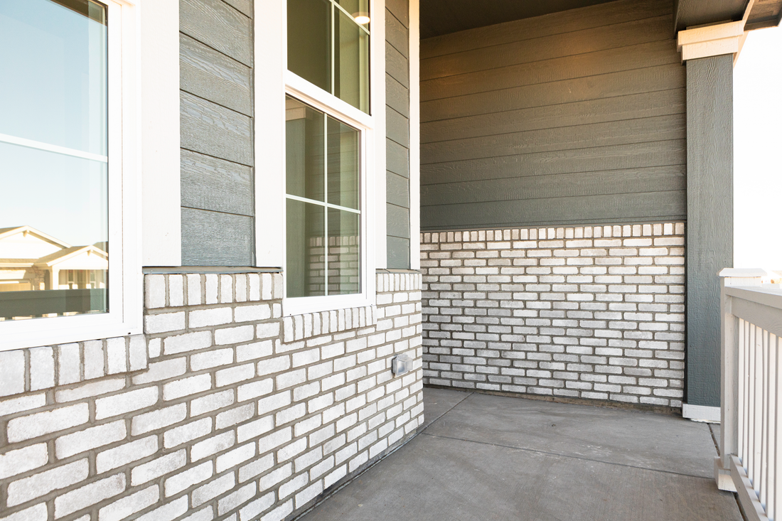 Light tumbled-edge thin brick below windows on a covered front porch, featuring Sunset Stone Storm Cloud Tumbled Edge Thin Brick.