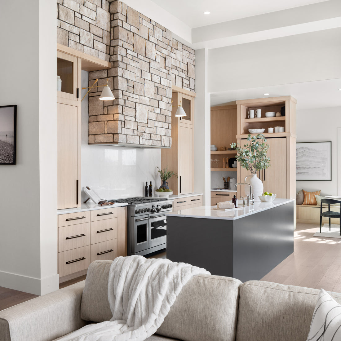 Pale limestone around a tall kitchen range hood beside cream cabinetry and a dark island, featuring Sunset Stone Winter Sky Limestone.