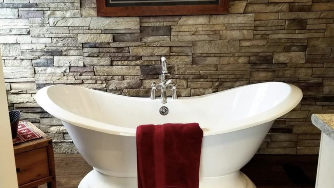 Freestanding white bathtub in front of a gray ledgestone bathroom wall, featuring Versetta Plum Creek Ledgestone.